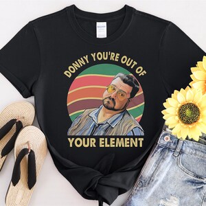 以下が含まれることがあります： 「Donny You're Out Of Your Element」というテキストと、サングラスをかけた男性のレトロなグラフィックがプリントされた黒いTシャツ。