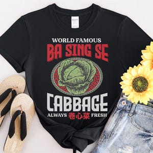 Pode incluir: Camiseta preta com um gráfico branco que diz "World Famous Ba Sing Se Cabbage Always  Fresh" com uma ilustração de couve verde em um círculo vermelho.