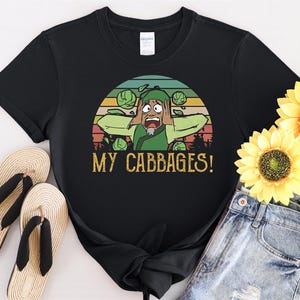 May include: Black t-shirt with a vintage-style graphic of a cartoon character with green hair and a green shirt, surrounded by green cabbages. The text "MY CABBAGES!" is printed below the graphic.