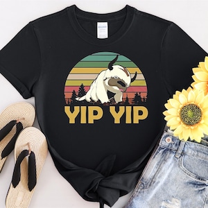 Könnte beinhalten: Schwarzes T-Shirt mit einem Retro-Grafikdruck eines weißen, pelzigen Wesens mit dem Text "Yip Yip" darunter.