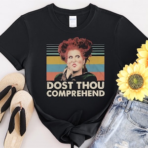 May include: Black t-shirt featuring a vintage-style image of a woman with red hair and a green dress. The text "Dost thou comprehend" is printed below the image.