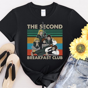 Op de afbeelding: Zwart T-shirt met een vintage-stijl grafische afbeelding van de personages uit The Breakfast Club. De afbeelding bevat de tekst "The Second Breakfast Club" en een retro-stijl achtergrond.