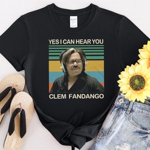 May include: Black t-shirt with a vintage-style graphic of a man wearing headphones and the text "YES I CAN HEAR YOU CLEM FANDANGO".