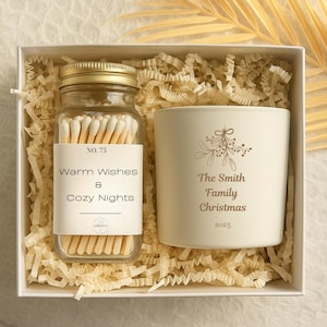 May include: A gift box containing a glass jar of matches and a white candle. The match jar has a gold lid and a label that reads "Warm Wishes & Cozy Nights." The candle is printed with "The Smith Family Christmas 2025."