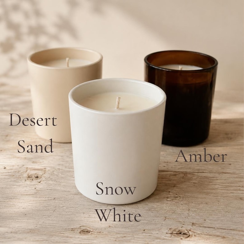 以下が含まれることがあります： ガラス容器に入った3本の円筒形キャンドル。マットベージュの「Desert Sand」、マットホワイトの「Snow White」、ダークブラウンガラスの「Amber」とラベルが貼られています。各キャンドルには中央にコットン製の芯が1本付いています。