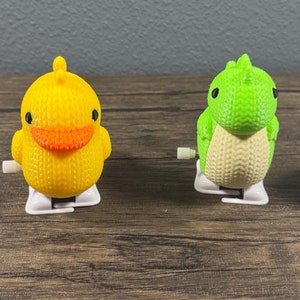 May include: Four wind-up toys, each with a different animal design. A black and white penguin with an orange scarf, a yellow duck, a green dinosaur, and a white chicken with a red comb.