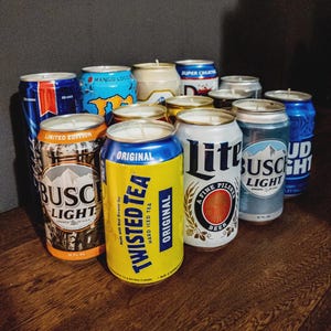 May include: A collection of beer and soda cans repurposed as candles. The cans feature various brand labels, including "Busch Light," "Twisted Tea," and "Bud Light." The candles have white wax and wicks.