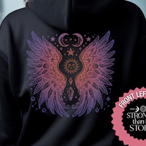 Puede incluir: Una sudadera con capucha negra con un diseño degradado en morado y rosa de alas, un sol, una luna y estrellas. El texto "Stronger than the storm" está en un círculo rosa.
