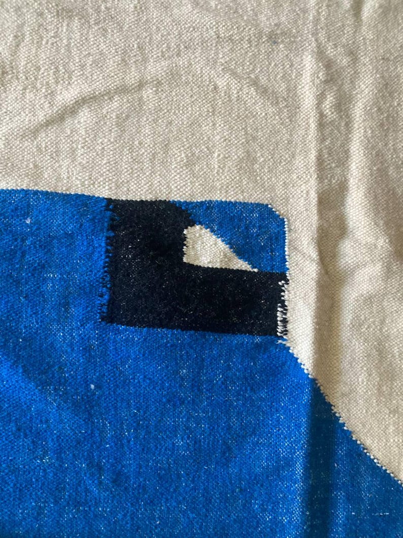 Peut inclure: Gros plan sur un tapis tiss&eacute; avec un motif g&eacute;om&eacute;trique. Le tapis est fait de fibres naturelles et pr&eacute;sente une palette de couleurs blanche, bleue et noire.