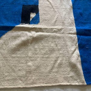 Peut inclure: Un tapis tiss&eacute; blanc, bleu et noir avec un motif g&eacute;om&eacute;trique. Le tapis a un centre blanc avec des rayures bleues et noires sur les bords.