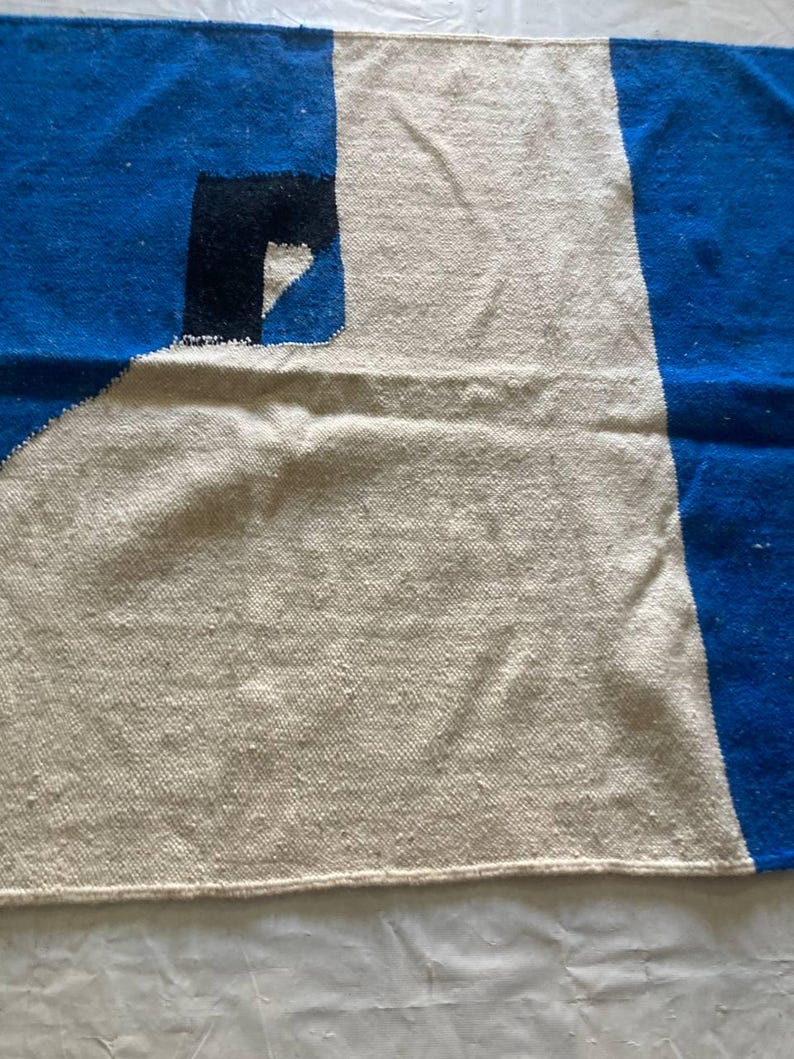 Peut inclure: Un tapis tiss&eacute; blanc, bleu et noir avec un motif g&eacute;om&eacute;trique. Le tapis a un centre blanc avec des rayures bleues et noires sur les bords.