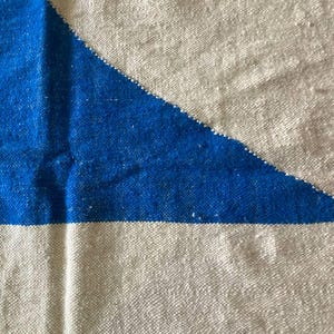 Peut inclure: Gros plan sur un tissu tiss&eacute; avec un motif g&eacute;om&eacute;trique. Le tissu est blanc avec un triangle bleu au centre. Le tissu a une texture rugueuse.