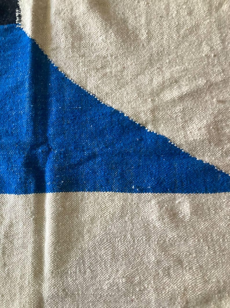 Peut inclure: Gros plan sur un tissu tiss&eacute; avec un motif g&eacute;om&eacute;trique. Le tissu est blanc avec un triangle bleu au centre. Le tissu a une texture rugueuse.