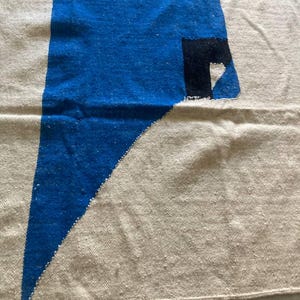 Peut inclure: Un tapis g&eacute;om&eacute;trique blanc et bleu avec une forme de c&oelig;ur noir et blanc dans le coin. Le tapis est fait d'un tissu tiss&eacute; et a une bordure frang&eacute;e.