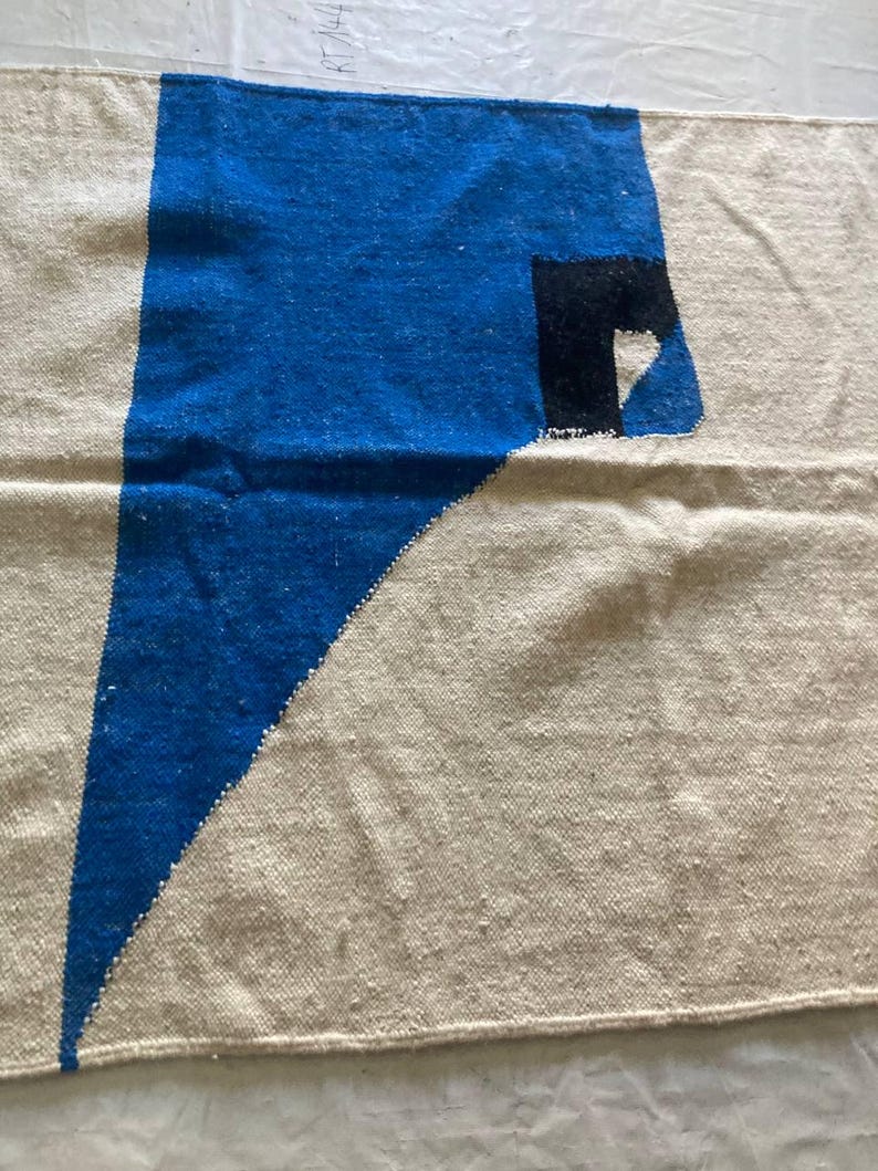Peut inclure: Un tapis g&eacute;om&eacute;trique blanc et bleu avec une forme de c&oelig;ur noir et blanc dans le coin. Le tapis est fait d'un tissu tiss&eacute; et a une bordure frang&eacute;e.