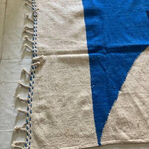 Peut inclure: Un tapis tiss&eacute; blanc et bleu avec des franges sur un c&ocirc;t&eacute;. Le tapis a un motif g&eacute;om&eacute;trique avec un grand triangle bleu.