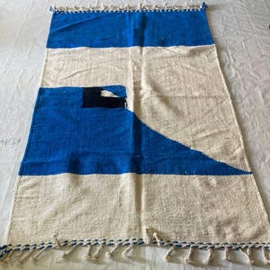 Peut inclure: Un tapis tiss&eacute; blanc et bleu avec un motif g&eacute;om&eacute;trique. Le tapis a des franges sur tous les c&ocirc;t&eacute;s.