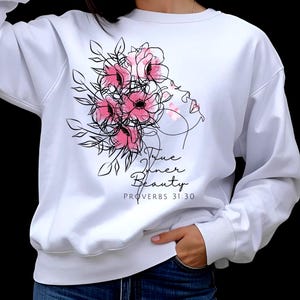 May include: White sweatshirt featuring a floral design with pink flowers and black line art of a woman's profile. The text "True Inner Beauty" and "Proverbs 31:30" are printed below the design. The sweatshirt has a crew neck and long sleeves.