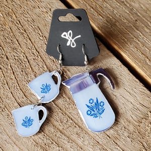 May include: A pair of silver earrings featuring a blue and white coffee pot and two cups with a blue floral design.