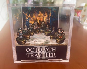 May include: A clear acrylic display case featuring miniature character figurines from the video game "Octopath Traveler." The case has a printed backdrop and a black base with the game's title in white text. The figurines are on decorative bases.