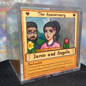 May include: A clear acrylic block featuring a pixelated image of a couple with the text "The Anniversary" and "Jamie and Angela." The image includes a heart and a rose, with the text "Soulmates" and a message about love and adventures.