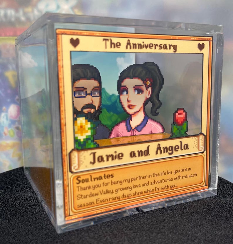 May include: A clear acrylic block featuring a pixelated image of a couple with the text "The Anniversary" and "Jamie and Angela." The image includes a heart and a rose, with the text "Soulmates" and a message about love and adventures.