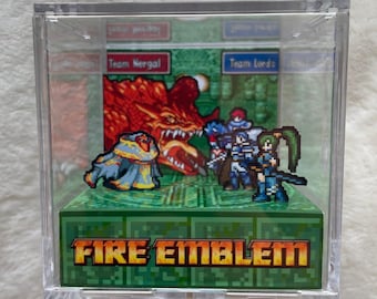 May include: A clear acrylic display case featuring a pixelated diorama of a scene from Fire Emblem. The scene includes a red dragon, characters, and the text "FIRE EMBLEM" in orange. The background is green.