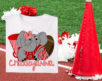 May include: White t-shirt featuring a cartoon elephant in a football uniform, a football, and a megaphone. The elephant has a red and white striped bow and is holding a pom-pom. The name "Charkeyanna" is written in red script.