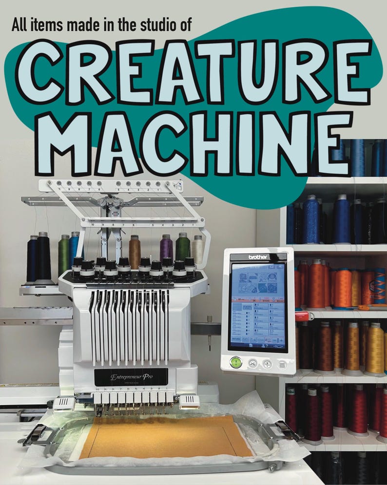 May include: A white and silver Entrepreneur Pro embroidery machine with a Brother control panel. The image features the text "CREATURE MACHINE" and shelves of colorful thread spools. The machine is set up with a tan fabric piece.