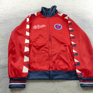 May include: A red zip-up jacket with a navy blue collar, cuffs, and hem. White and navy blue triangles decorate the sleeves. The jacket has a logo on the chest and the word "Superior" in script on the chest.