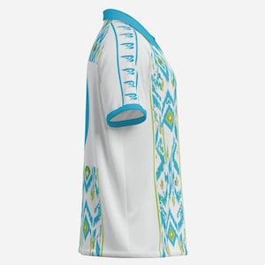 May include: White short-sleeved shirt with a turquoise collar and sleeve trim. The shirt features a repeating geometric pattern in turquoise and green. The design is reminiscent of tribal or ethnic textiles.