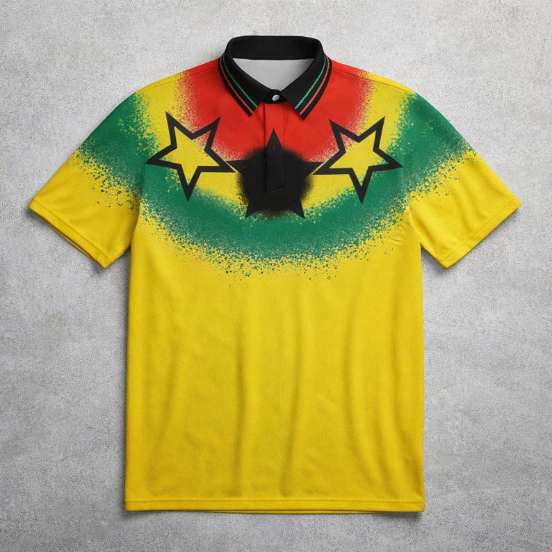 Puede incluir: Polo amarillo con cuello negro y mangas cortas. La camisa presenta un dise&ntilde;o con efectos de pintura en aerosol roja, verde y negra, junto con tres formas de estrella negra.