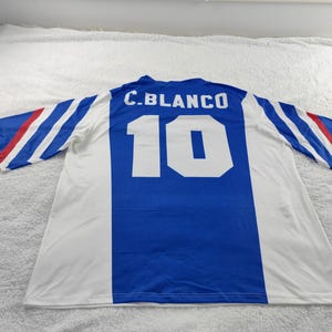 May include: A white, blue, and red soccer jersey with the name "C. BLANCO" and the number "10" on the back. The jersey has blue and white sleeves with red and white stripes. The jersey is laid flat on a white surface.