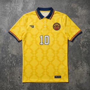 Könnte beinhalten: Gelbes Fußballtrikot mit geometrischem Muster und der Nummer 10. Das Trikot hat einen marineblauen Kragen und Ärmelbesatz mit roten Akzenten. Mit dem Ecuador-Emblem und einem kleinen Logo auf der Brust.
