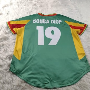 May include: Green jersey with yellow and red detailing. The back displays the name "BOUBA DIOP" above the number "19" in white. The jersey has a round neck and short sleeves.