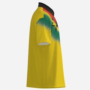 Puede incluir: Polo amarillo con cuello negro, rojo y verde. La camiseta presenta un dise&ntilde;o con los colores de la bandera de Ghana, incluida una estrella negra. La camiseta tiene mangas cortas y un ribete blanco.