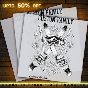 May include: A black and white DTF transfer sheet featuring a graphic of crossed skis, ski poles, and goggles with a mountain scene. The design includes snowflakes and stars, with the text CUSTOM FAMILY and Custom City, State.