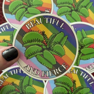 May include: A round sticker featuring a green Venus flytrap illustration with the text "BEAUTIFUL AND FIERCE." The background has a rainbow stripe design. Several stickers are visible.