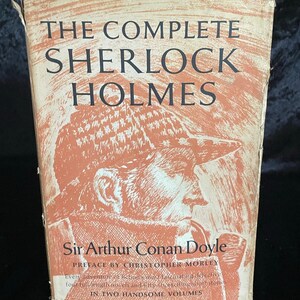 May include: A vintage copy of "The Complete Sherlock Holmes" by Sir Arthur Conan Doyle. The book cover features an illustration of Sherlock Holmes in profile, with text in a serif font. The cover has a faded orange and cream color scheme.