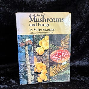 May include: A vintage book titled "all color book of Mushrooms and Fungi" by Moira Savonius. The cover features colorful illustrations of various mushrooms and fungi. The book's cover is a light tan color with black and brown text.