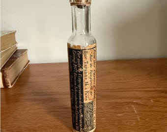 May include: A vintage glass bottle with a cork stopper and a label that reads "Eau des Carmes déchaussées de la Rue de Vaugirard, Rue Taranne 14, à Paris". The label is printed in black ink on a cream-colored background.