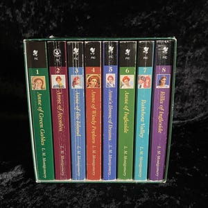 Op de afbeelding: Een boxset van acht boeken uit de "Anne of Green Gables" serie van L.M. Montgomery. De ruggen zijn in verschillende kleuren, met portretten van vrouwen. Titels zijn onder meer "Anne of Green Gables", "Anne of Avonlea" en "Rilla of Ingleside".