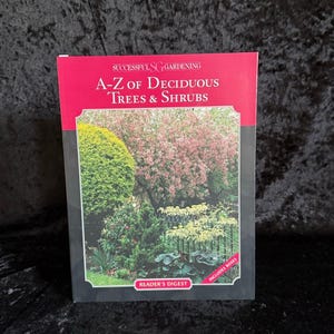 Może przedstawiać: Książka zatytułowana "A-Z of Deciduous Trees & Shrubs" autorstwa Reader's Digest. Okładka książki przedstawia kolorowe zdjęcie ogrodu z różnymi drzewami i krzewami. Książka jest częścią serii "Successful Gardening" i zawiera róże.