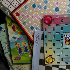May include: A collection of board games, including Scrabble, Sorry!, and a game called "No Stress Chess". The games are laid out on a black and white checkered surface.