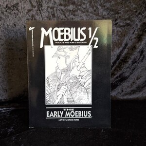 May include: Black and white cover of a comic book titled "Moebius 1/2 The Black & White Work of Jean Giraud The Early Moebius & Other Humorous Stories". The cover features a black and white illustration of a person wearing a helmet and armour holding a spear.