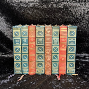 May include: A collection of vintage books with teal and red covers. The spines feature gold lettering and decorative patterns. Titles include "Kenilworth," "The Talisman," and "Adam Bede." The books are from the International Collectors Library.