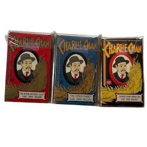 May include: Three vintage Charlie Chan books in red, blue, and black. Each book cover features a portrait of Charlie Chan in a hat and suit, with the title "Charlie Chan" above and the book title below.