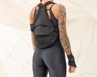 May include: A person wearing a black jumpsuit with a black backpack, black boots, and black wristbands. The person has braided hair and tattoos on their arm.
