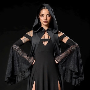May include: Black hooded dress with long sleeves and high slits. The dress features a cape-like overlay and lace accents on the sleeves. The model is wearing black platform boots. The overall style is gothic and elegant.