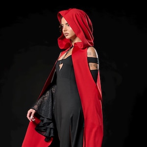 May include: A long, flowing black dress with a matching red hooded cape. The cape has a deep red exterior and a black interior. The sleeves of the dress are black lace. The outfit is set against a black background.